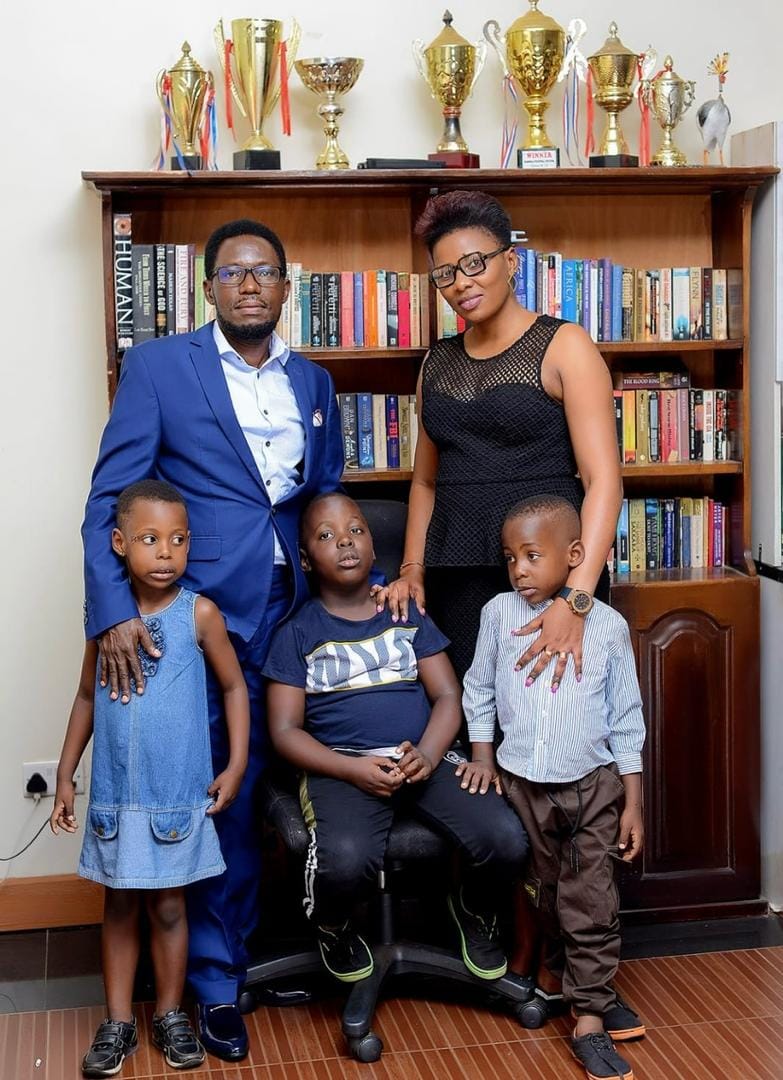 Valentino Kamya with his wife and children beside a bookshelf of trophies