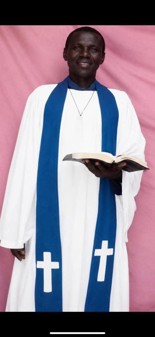 Valentino Kamya in clergy vestments holding an open Bible